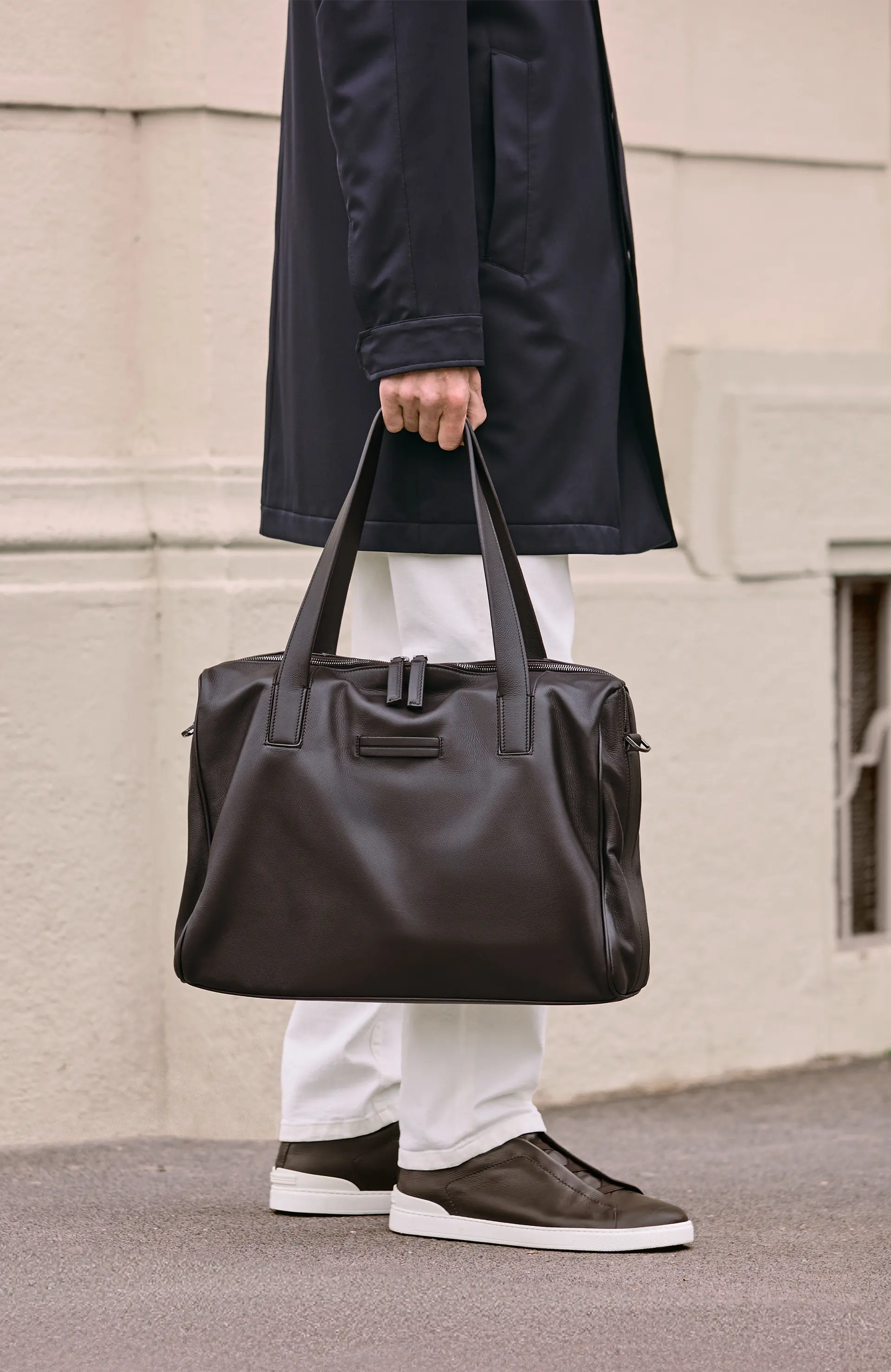 手持奢华皮革包袋、身穿 ZEGNA(杰尼亚)2025 秋冬系列风衣的一位男士。