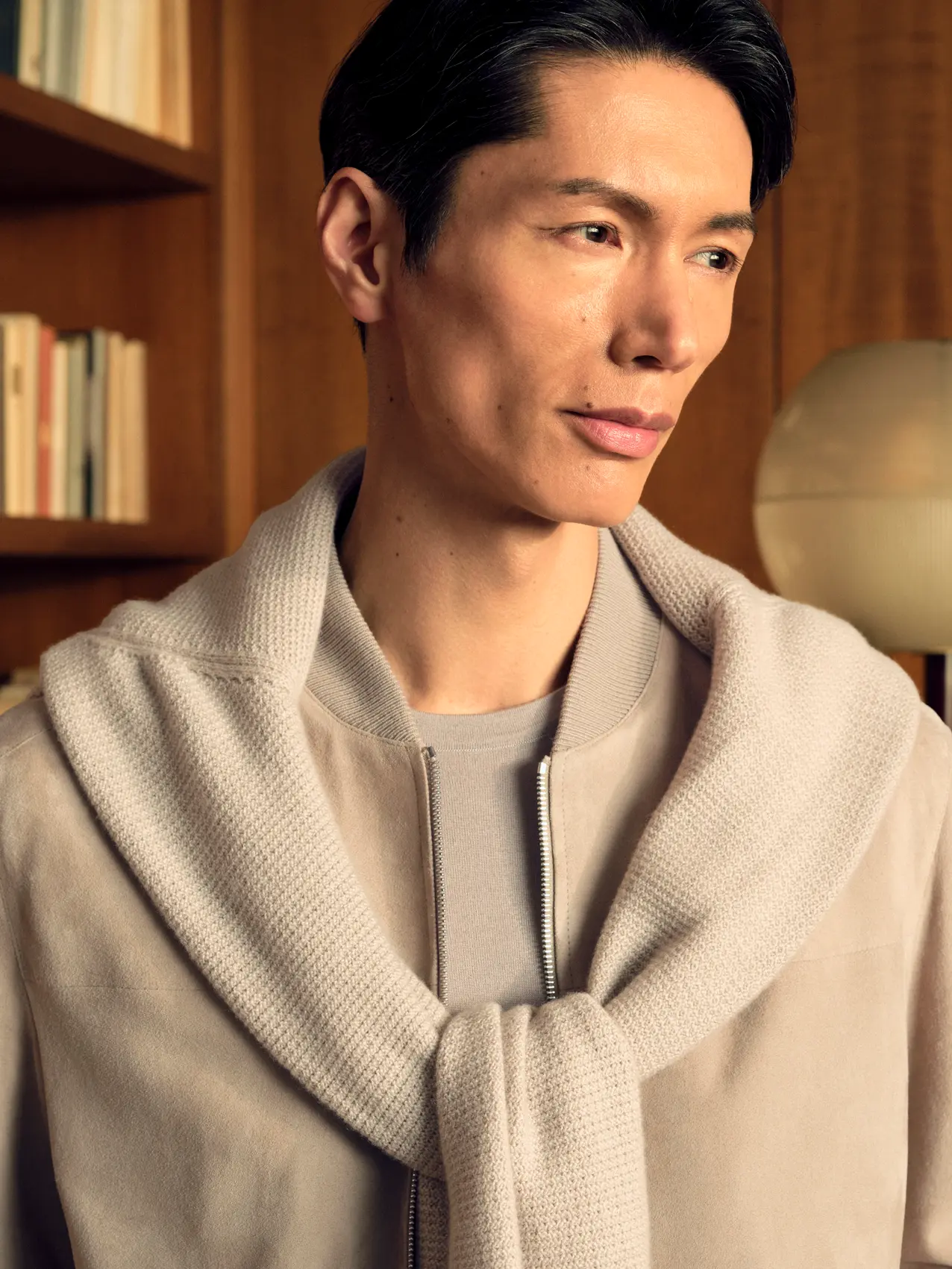 Close-up of a man wearing the lamb suede bomber in light taupe with an Oasi Cashmere zip mock draped over the shoulders and a Cashseta crewneck underneath, from the ZEGNA FW26 collection.
