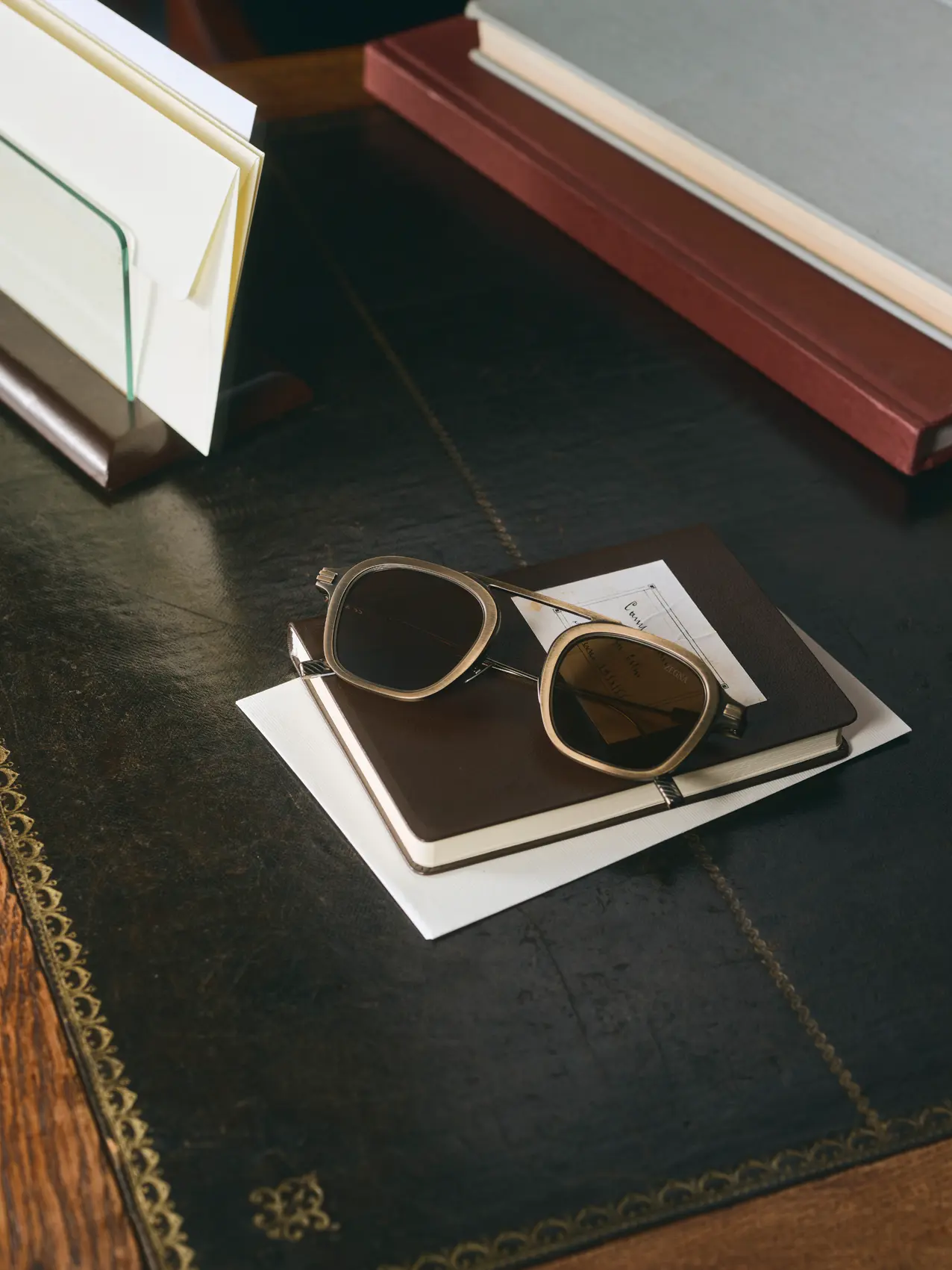 Zegna titanium sunglasses resting on a notebook on an elegant leather-top desk.