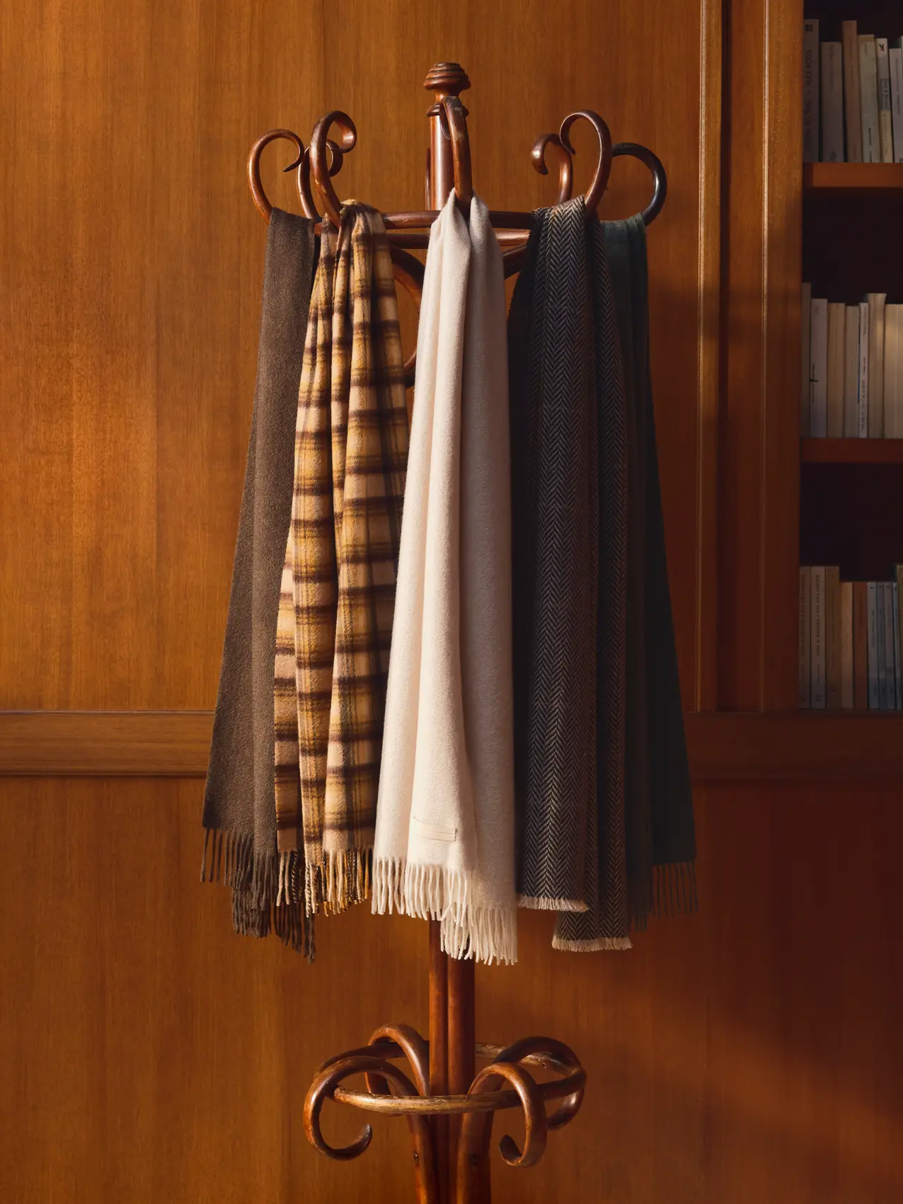 Four fringed wool scarves in brown, mustard plaid, ivory, and gray herringbone hanging on a bentwood coat rack, from ZEGNA Fall/Winter 2026 collection.