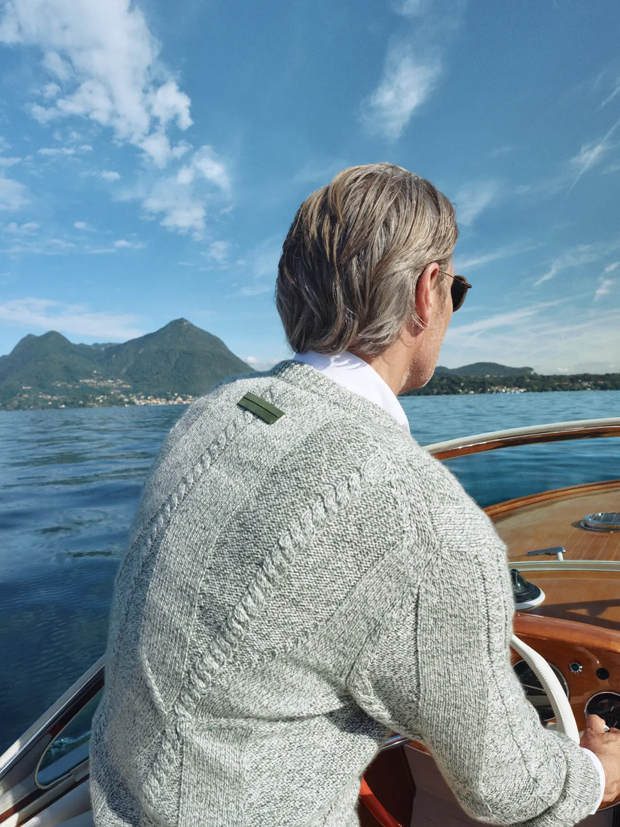 Close-up of Mads Mikkelsen on a boat by the lake wearing a grey V-neck sweater from the ZEGNA Spring Summer 2026 collection