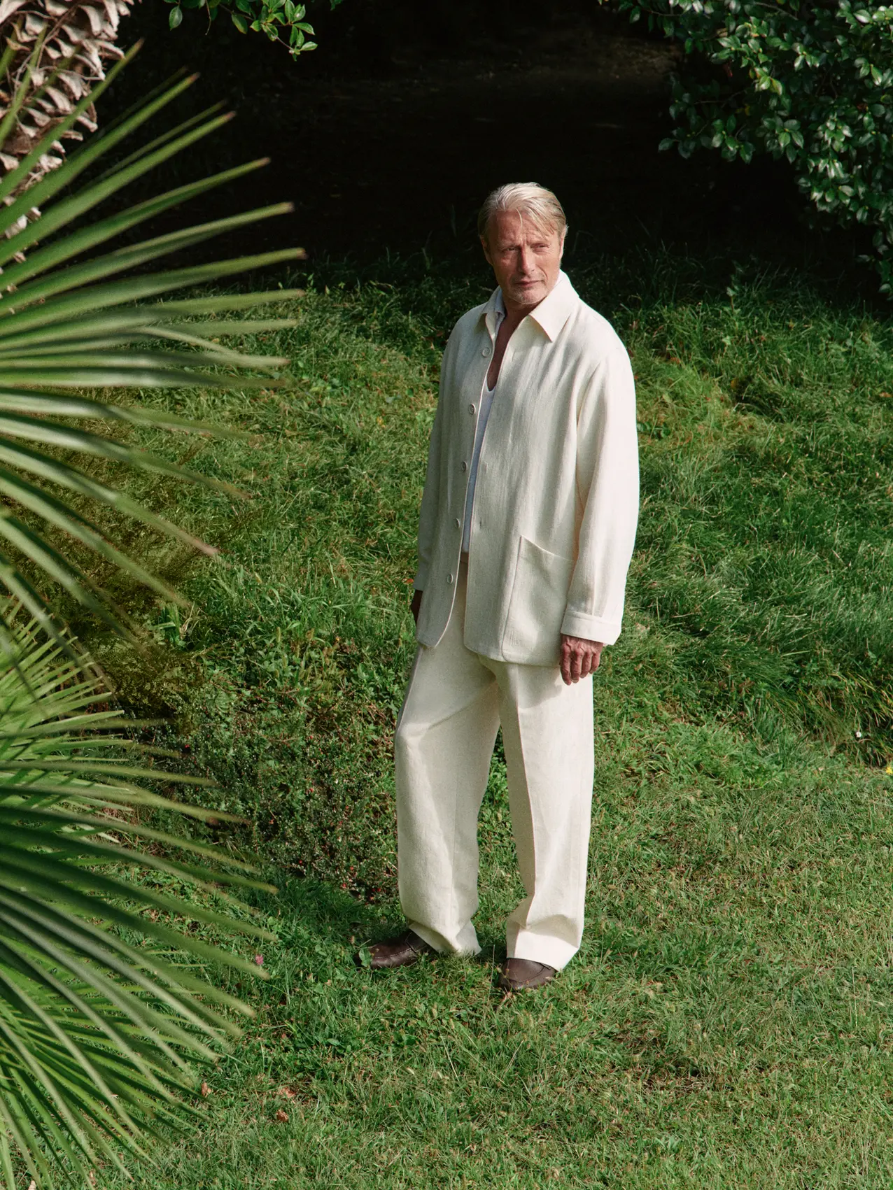 Mads Mikkelsen wearing a refined look from the ZEGNA Spring Summer 2026 collection in a lakeside garden setting.