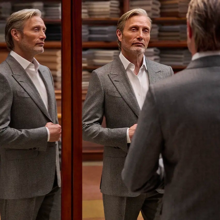 Mads Mikkelsen in a refined grey tailored suit with a white shirt, seen in full in the triple mirror of a tailoring atelier, from the ZEGNA Fall/Winter 2026 collection.