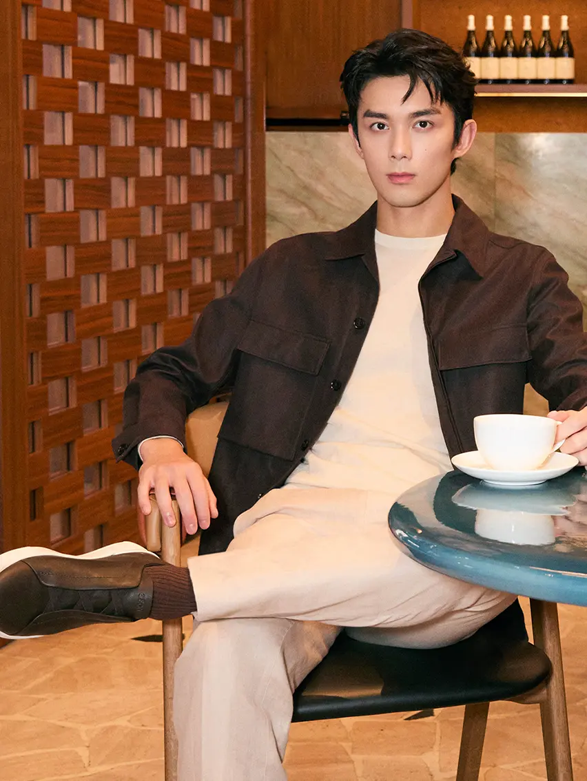 Wu Lei sitting at the ZEGNA Shanghai Taikoo Café, wearing a black overshirt and Triple Stitch sneakers.