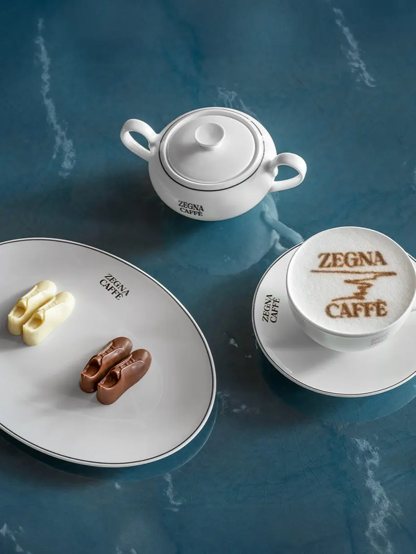 A blue table with a cappuccino bearing the ZEGNA Café logo and snacks shaped like sneakers, offered in the ZEGNA Café in Shanghai.