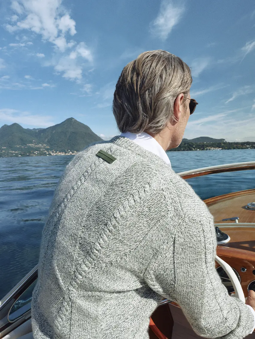 Mads Mikkelsen 在湖邊船上穿著 ZEGNA 2026 春夏系列灰色 V 領毛衣的特寫。
