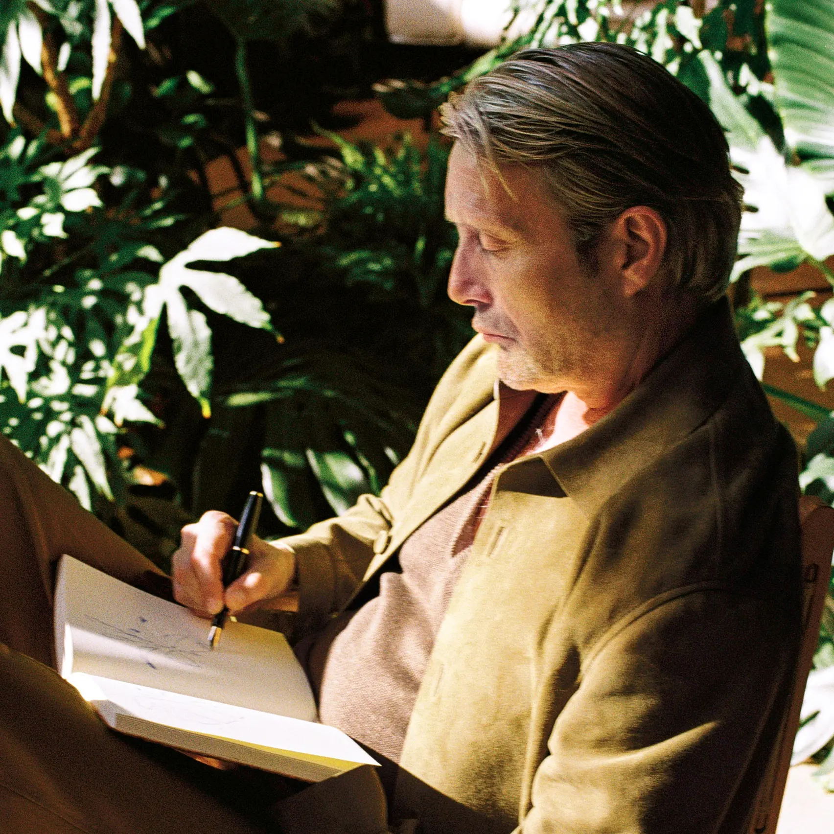 Mads Mikkelsen in a ZEGNA SS26 outfit, sketching ideas in a notebook during a quiet creative moment.