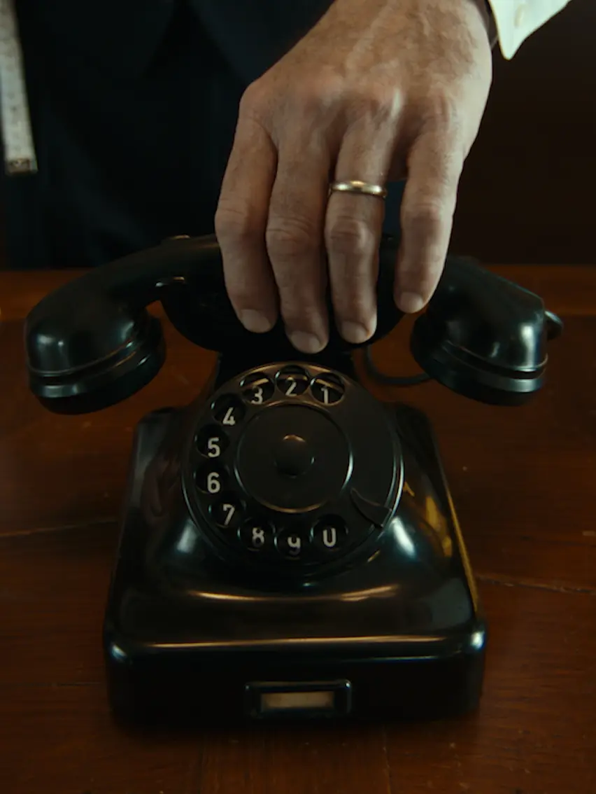 Close-up of a hand lifting the receiver of a black rotary telephone.