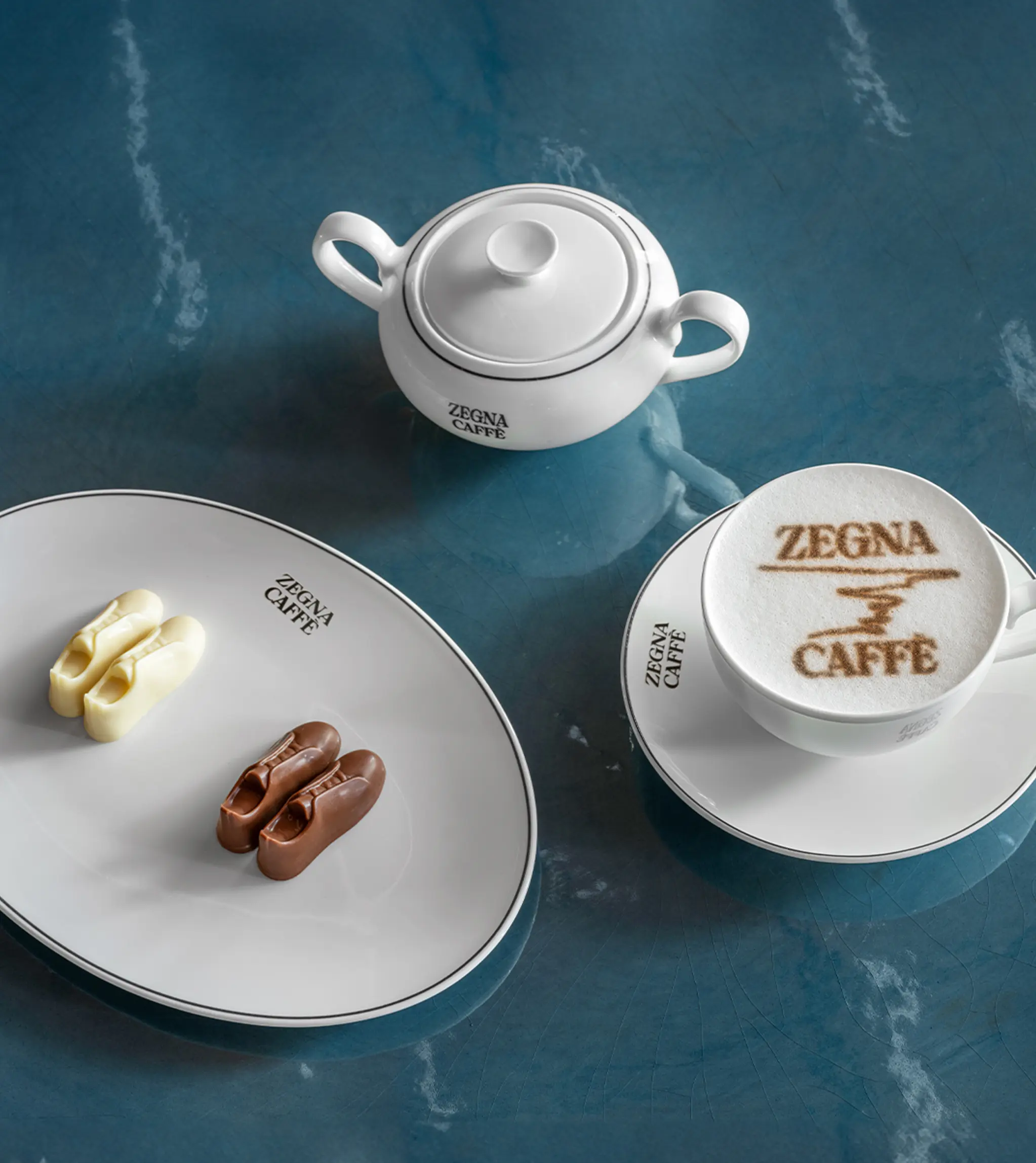 A blue table with a cappuccino bearing the ZEGNA Café logo and snacks shaped like sneakers, offered in the ZEGNA Café in Shanghai.