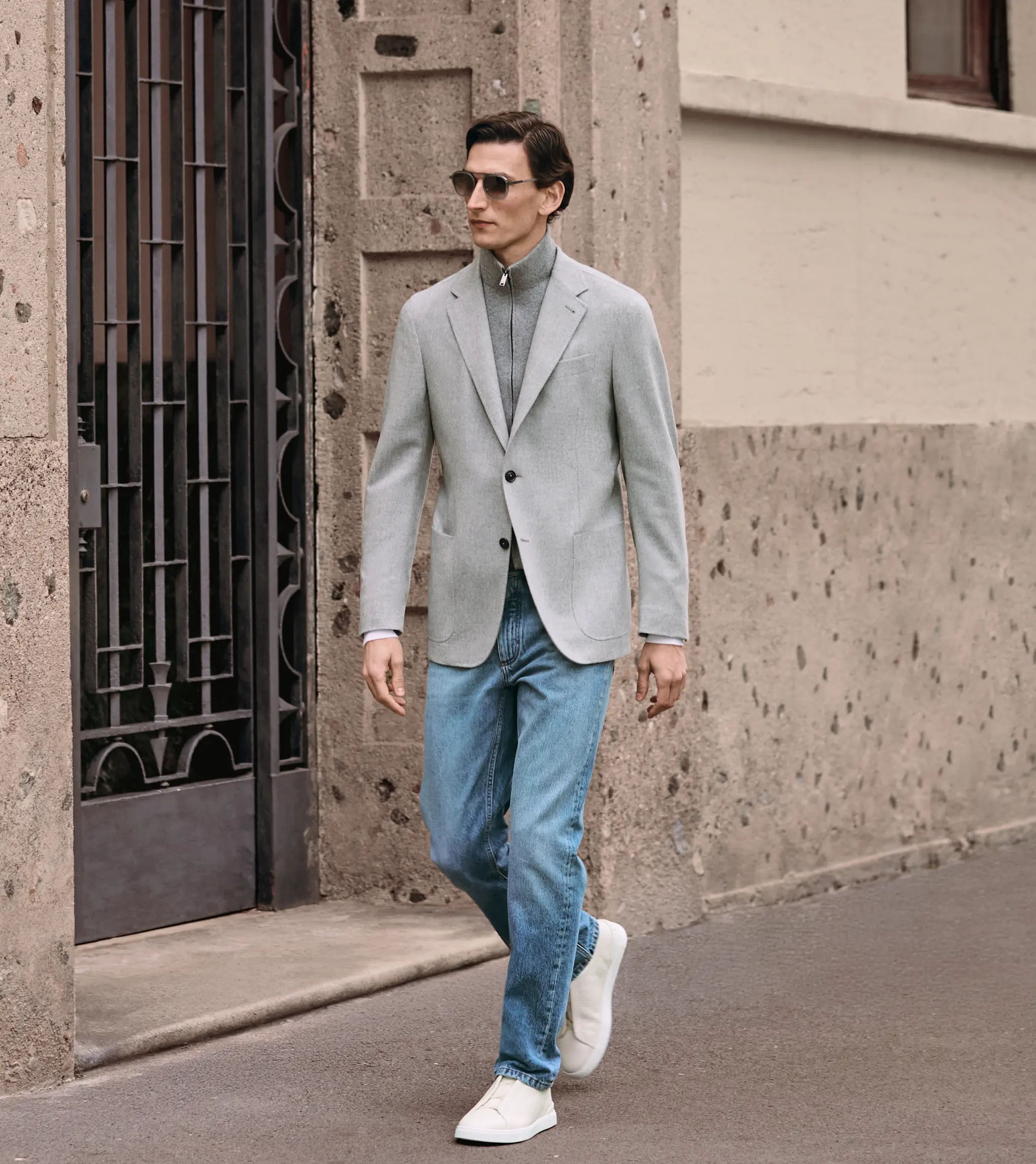 一位男士身着 ZEGNA（杰尼亚）FW25 系列服饰，包括一件休闲西装、一条牛仔裤和白色 Triple Stitch™ 运动鞋，打造精致休闲风格。