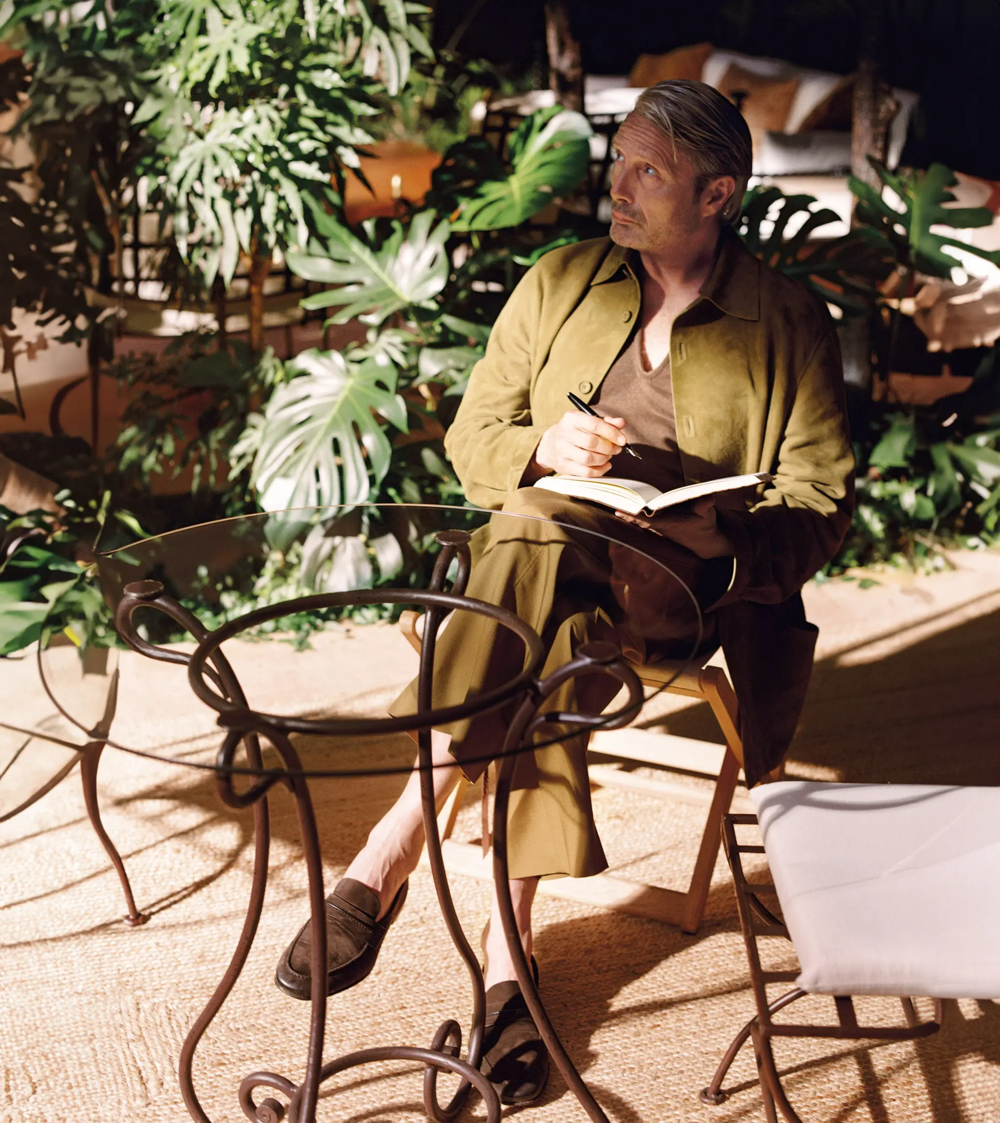 身穿 ZEGNA SS26 造型的麦斯·米科尔森，在安静的创作时刻于笔记本中勾勒灵感。