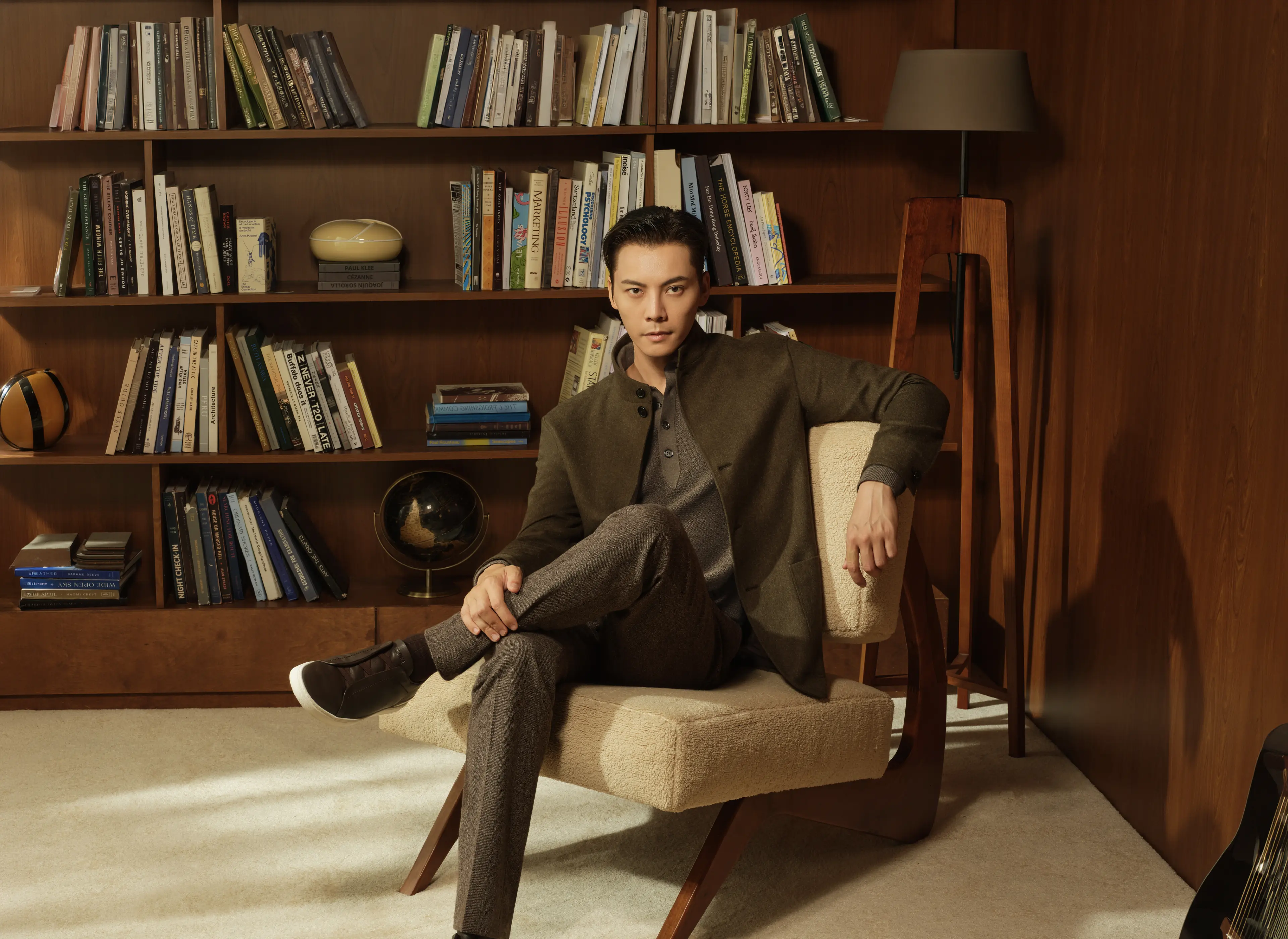 陈伟霆席地而坐，背靠书架，身着 Zegna FW26 精致冬日造型——Il Conte 夹克，Oasi Cashmere 面料，深橄榄绿多色混纺。