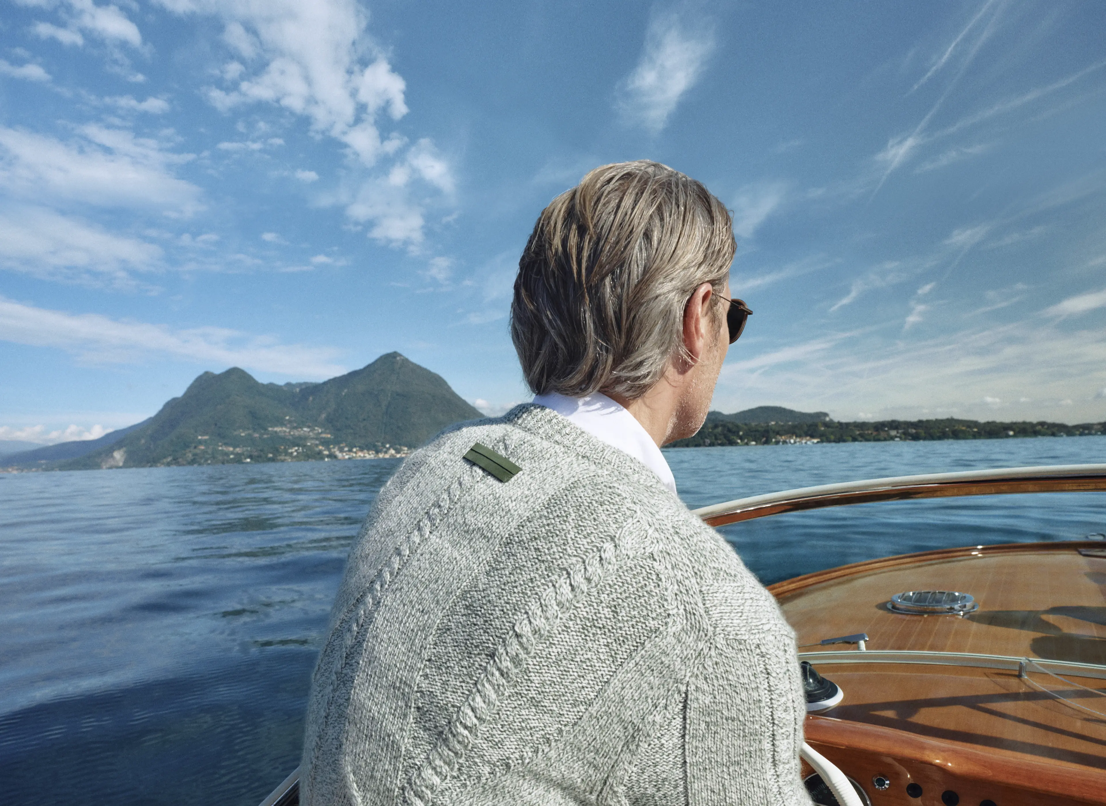 湖畔船上 Mads Mikkelsen 的特写，他身穿来自 ZEGNA（杰尼亚）2026 春夏系列的灰色 V 领毛衣。
