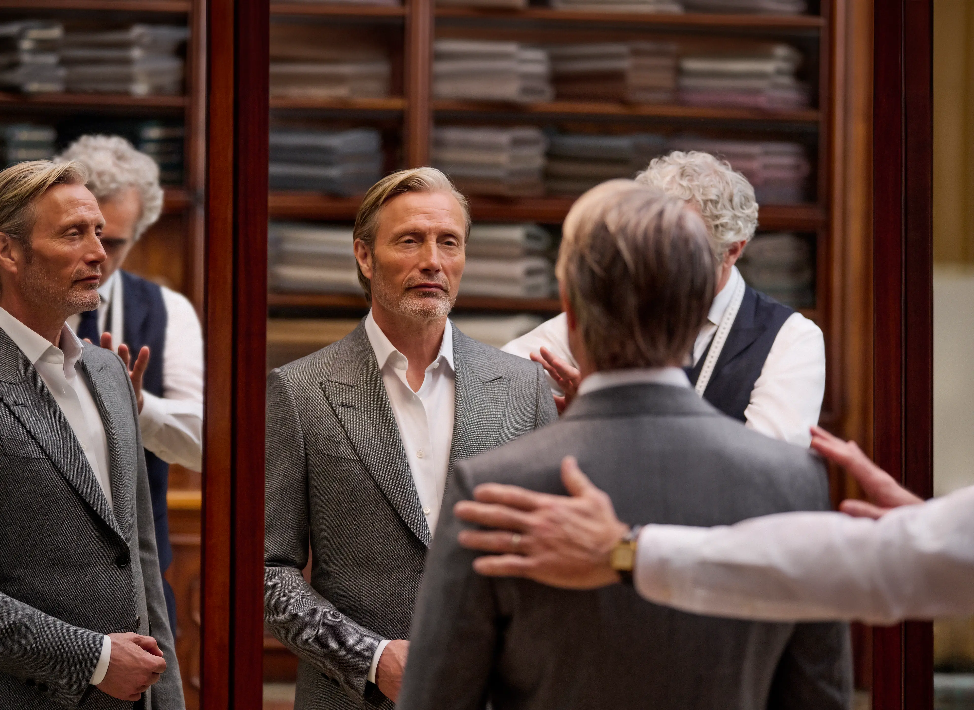 Mads Mikkelsen in a grey tailored suit being fitted by a tailor in an atelier, reflected in the fitting room mirrors, from the ZEGNA Fall/Winter 2026 collection.