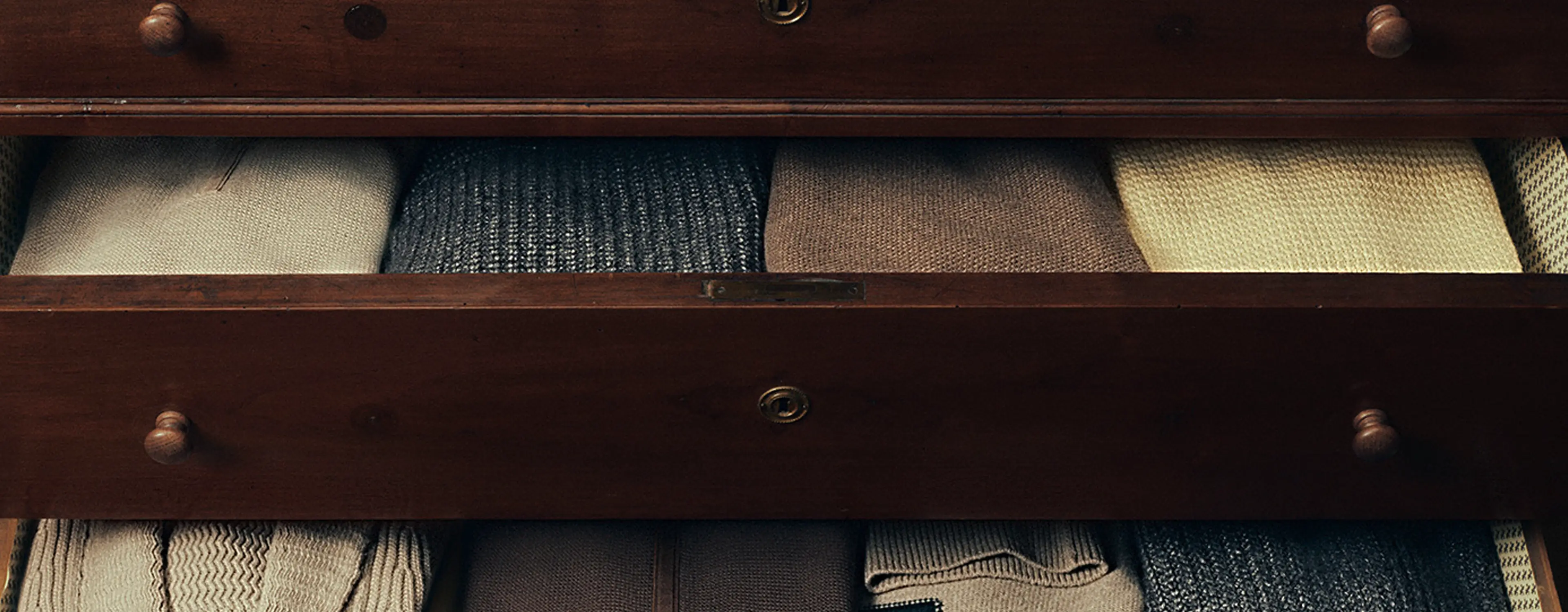 Stacked ZEGNA men’s sweaters in fine wool and luxury fabrics, folded in a wooden wardrobe.