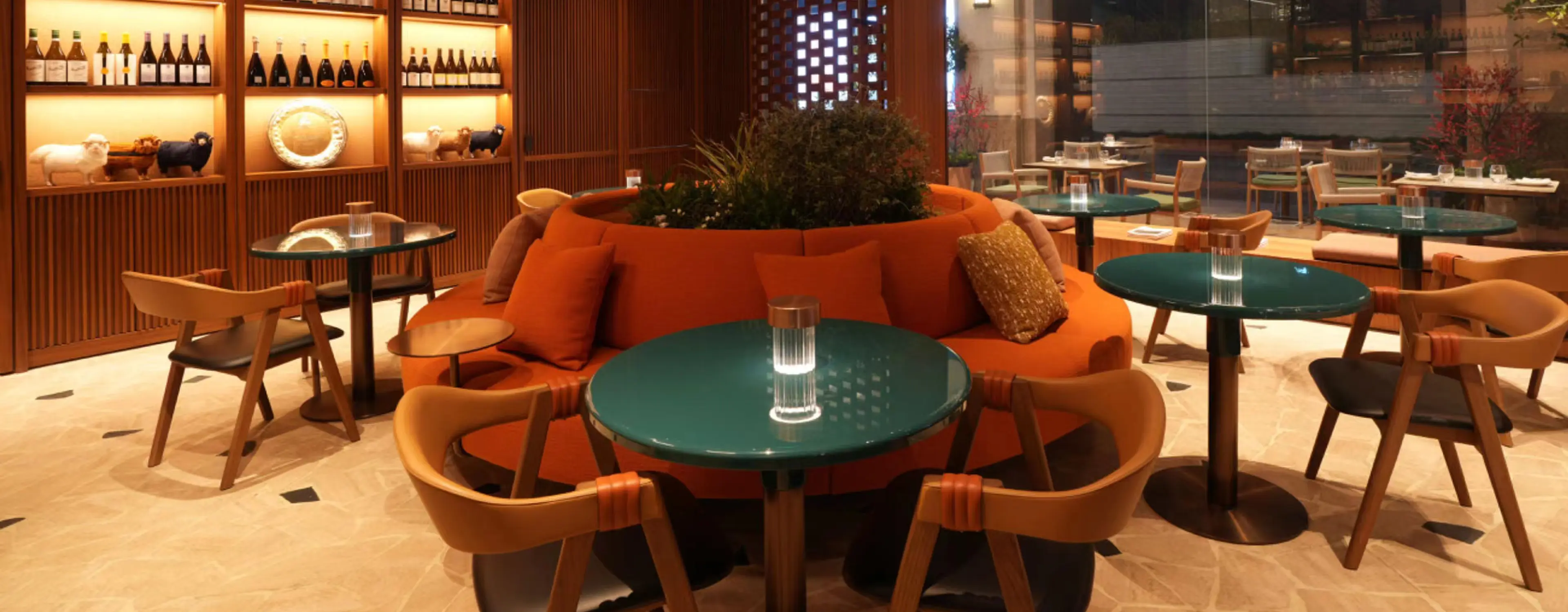 The interior of the ZEGNA Café in Shanghai, featuring modern decor with orange couches, green tables, wooden chairs, and a central plant arrangement.