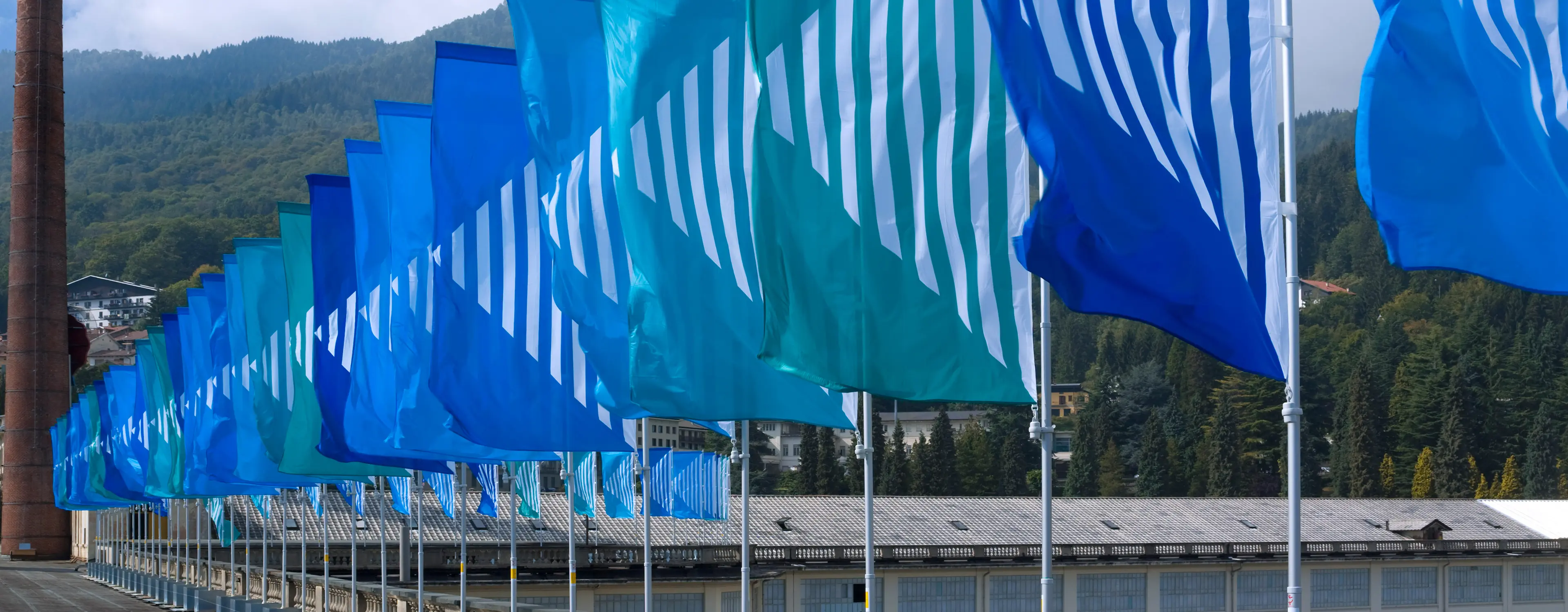 A view of Art Basel in Basel, featuring a historic building, a tall brick chimney, and vibrant blue flags lining a walkway.