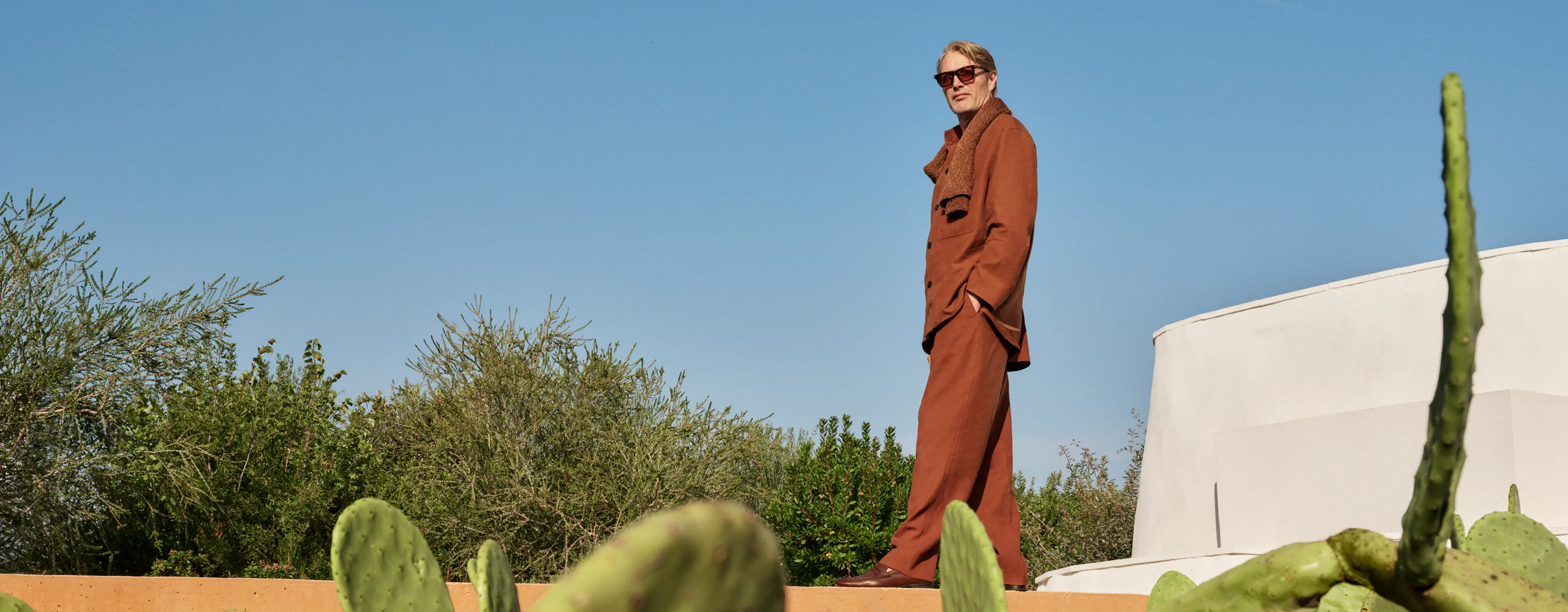 Mads Mikkelsen wearing a refined linen outfit in an earthy tone, paired with leather loafers, from the ZEGNA SS25 collection.