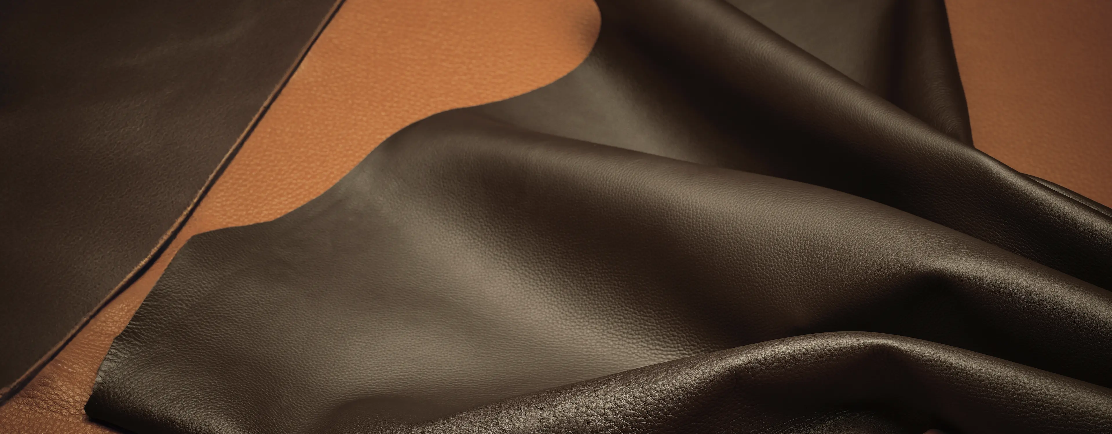 Close-up of a premium ZEGNA leather piece in dark brown, highlighting its soft, supple texture on a lighter brown background.