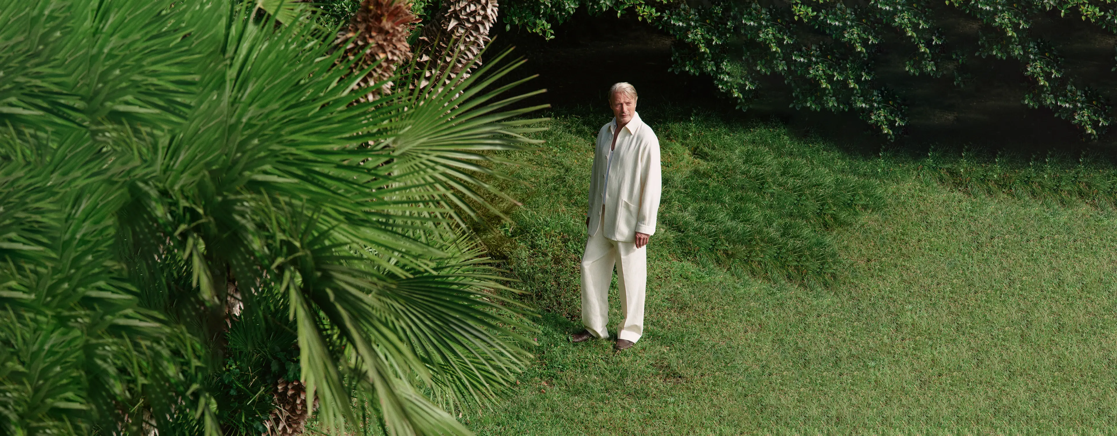 Mads Mikkelsen wearing a refined look from the ZEGNA Spring Summer 2026 collection in a lakeside garden setting.
