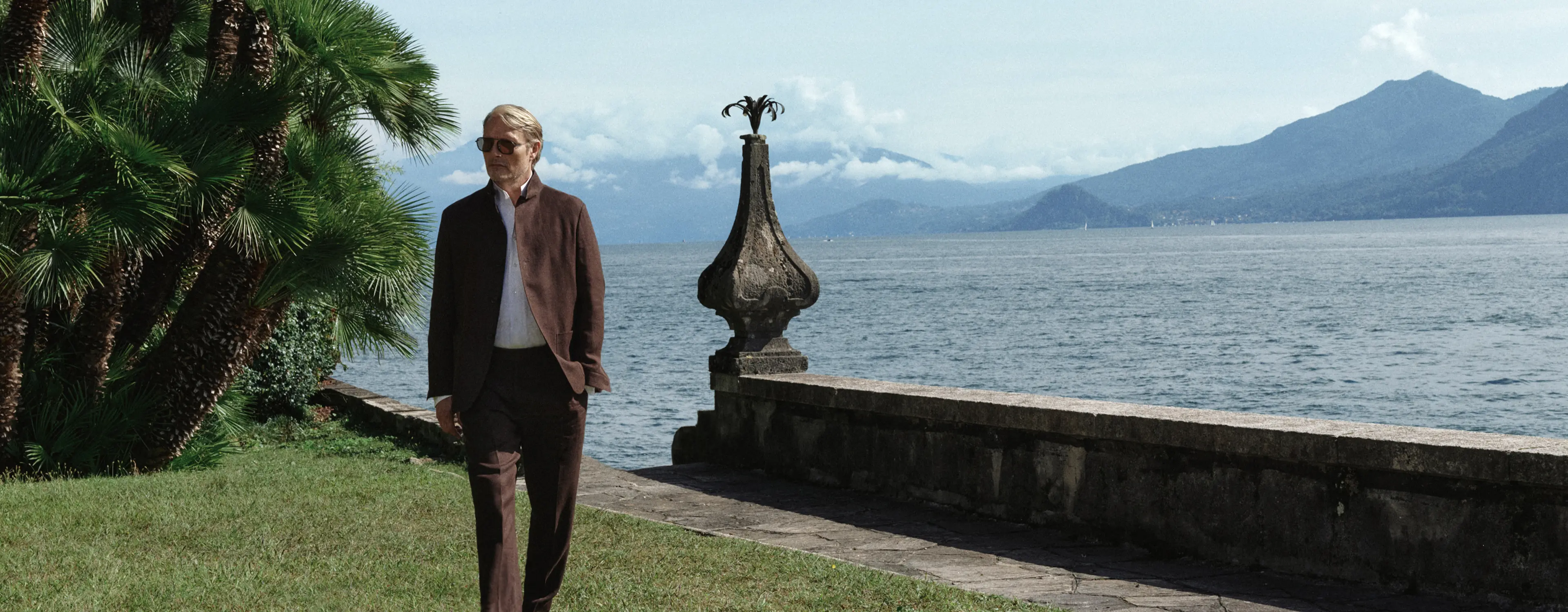 Mads Mikkelsen wearing a refined look from the ZEGNA Spring Summer 2026 collection in a lakeside garden setting.